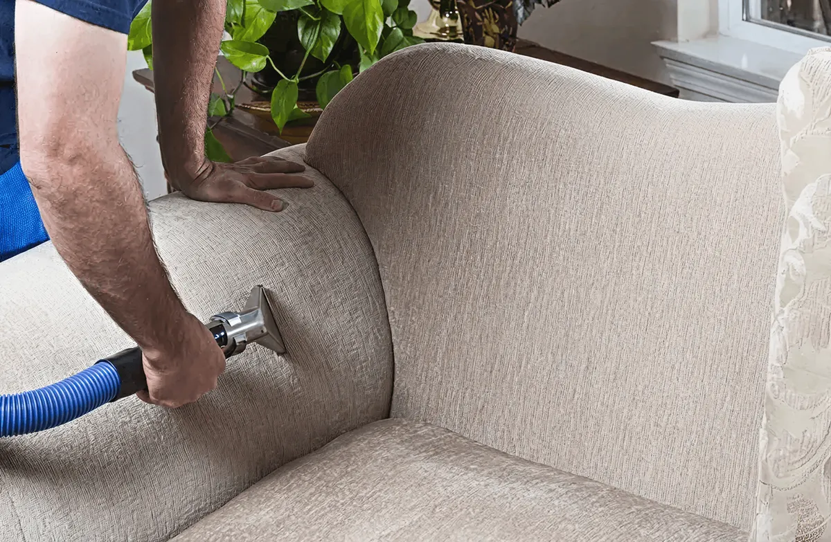 Professional upholstery cleaner deep-cleaning a fabric sofa with a handheld extraction tool and hose, Detroit, MI.